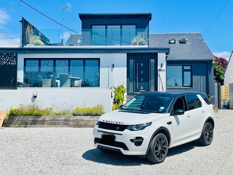 A white SUV parked in front of a Harbour Reach two-story house with large windows and a gravel driveway.