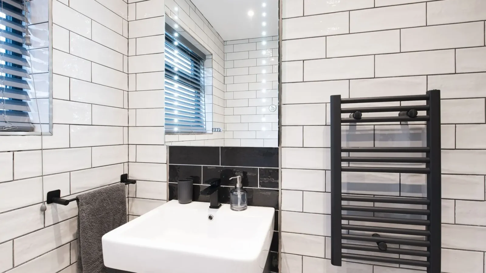 Modern bathroom with white subway tiles, a rectangular mirror, black fixtures, a towel rack, and a small sink within reach.