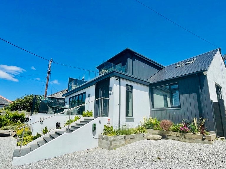 Modern Harbour Reach house with grey and white exterior, featuring a second-story balcony, surrounded by gravel and plants.