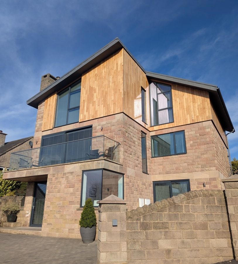 Oakwood House: A modern three-story with stone-wood facade, expansive windows, and balcony under a clear blue sky.