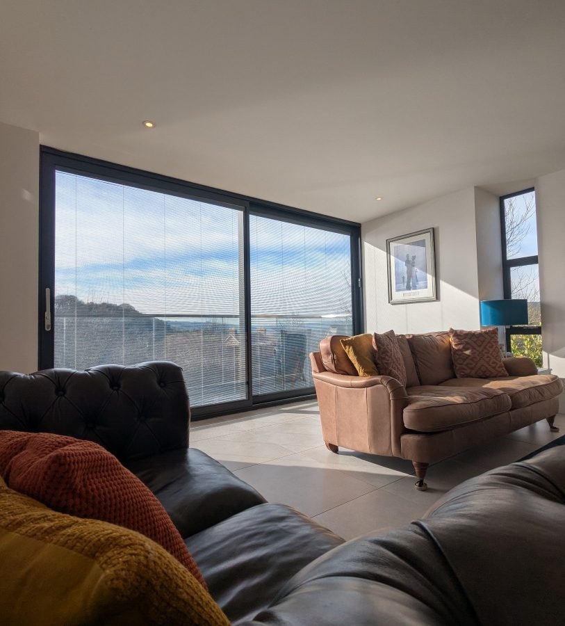 A modern living room at Oakwood House, featuring leather sofas, large sliding glass doors, and sunlight streaming in.