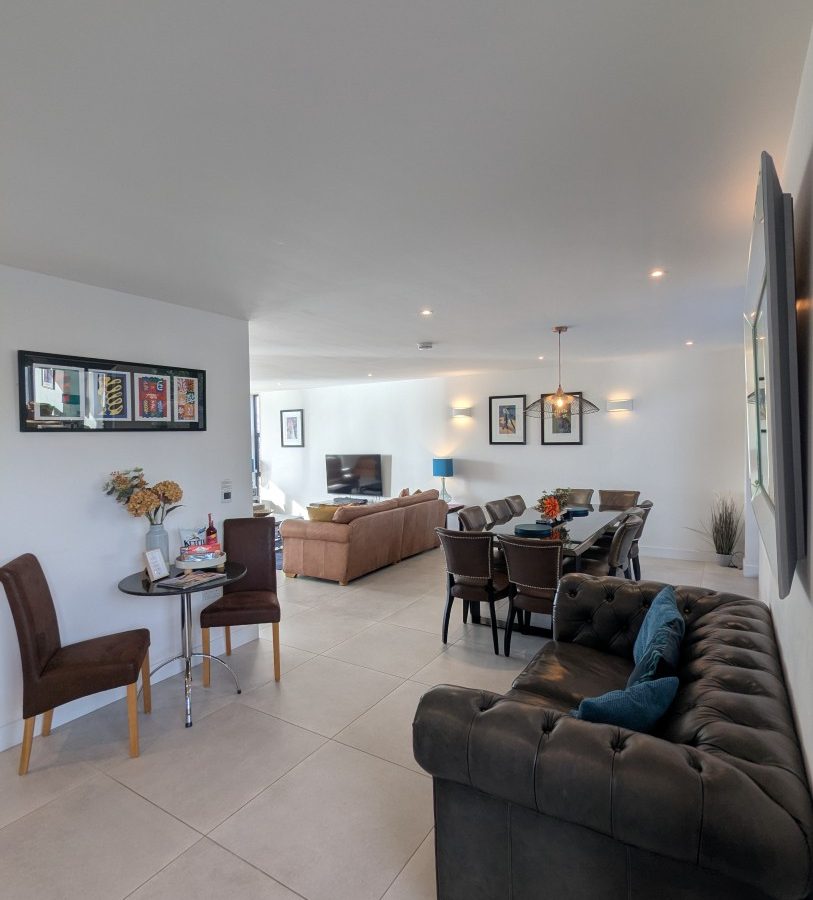 Open-plan living at Oakwood House, featuring a sofa, dining table, chairs, and wall art. Bright natural lighting fills the space.