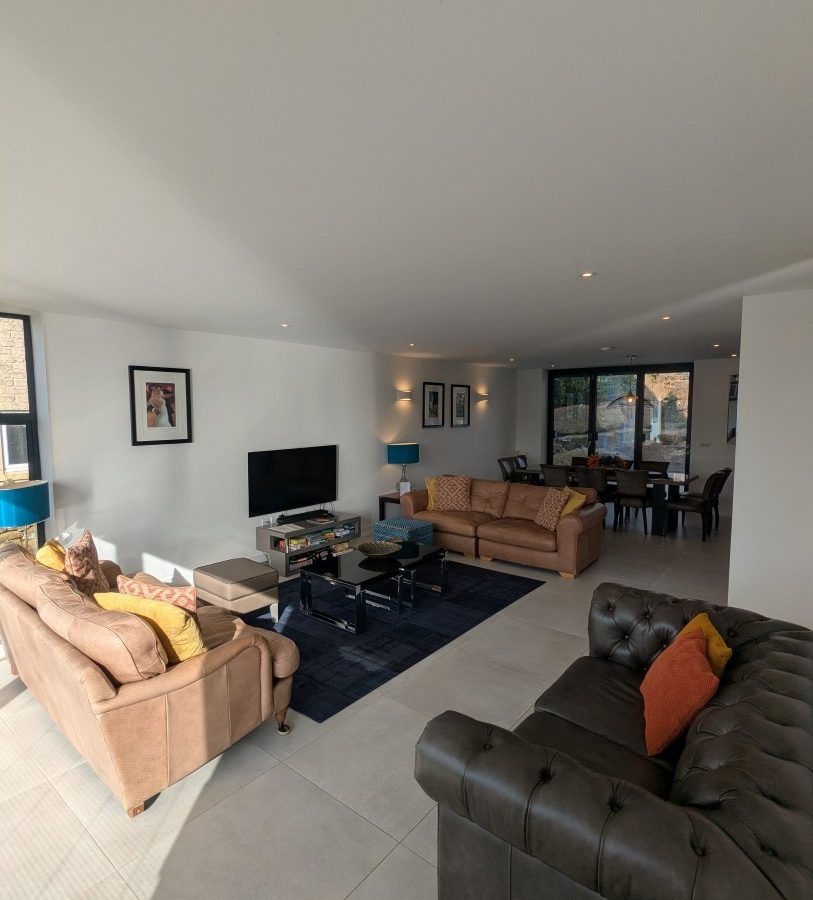 Spacious living room at Oakwood House, featuring two sofas, a TV, and dining area. Large windows fill it with natural light.