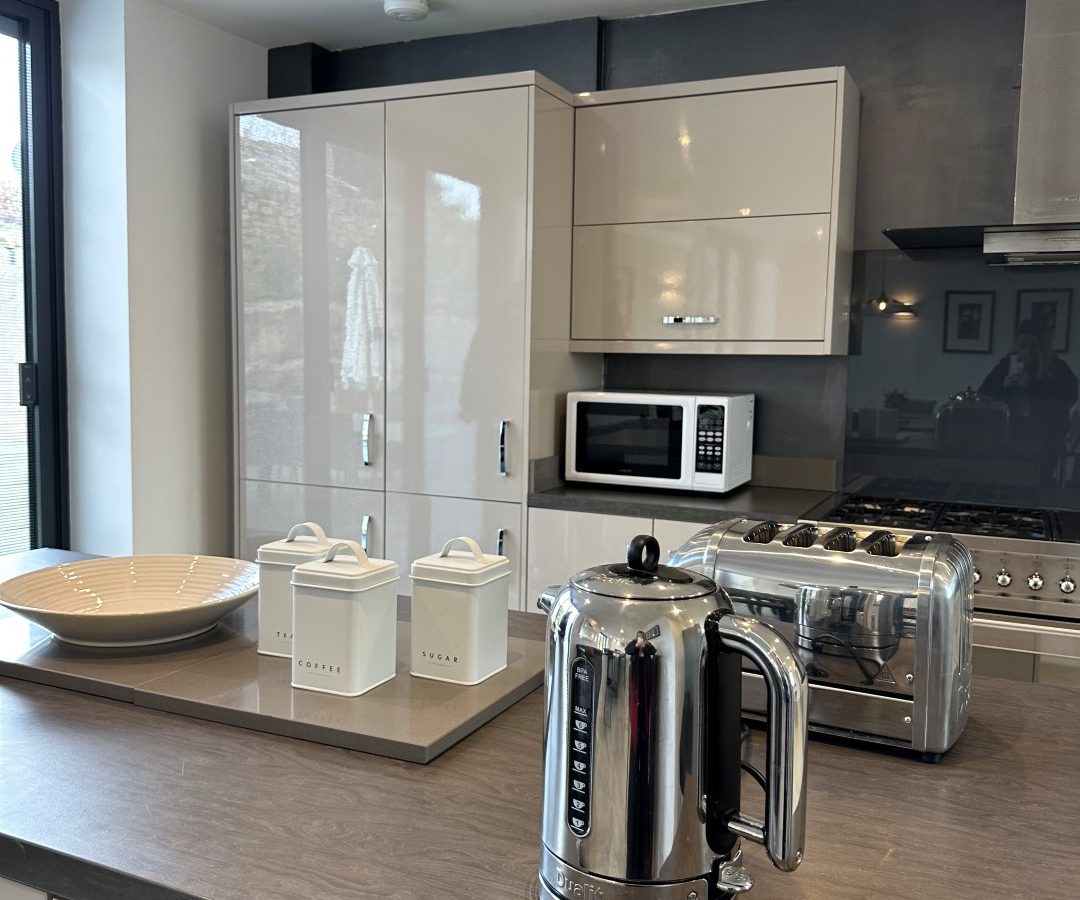 Modern kitchen at Oakwood House features gray cabinets, a toaster, an electric kettle, a microwave, and decorative containers on a wooden countertop.