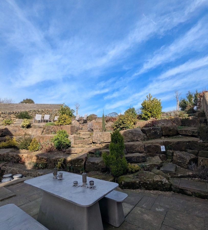 Outdoor patio at Oakwood House features a stone bench and table, with a stepped rock garden under the clear blue sky.