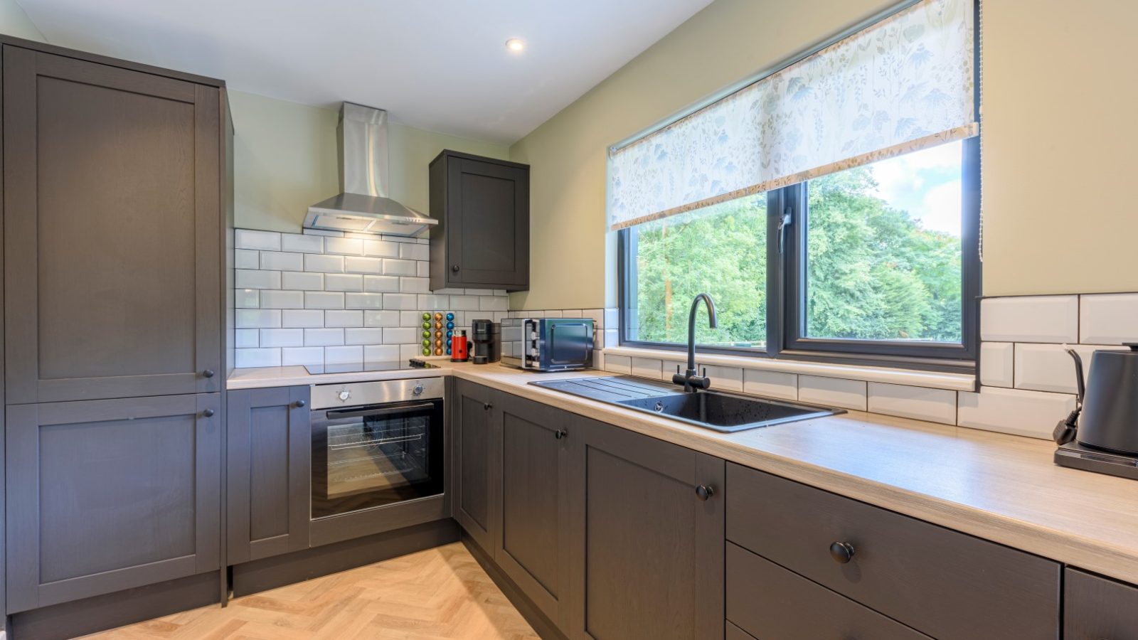 Modern kitchen with dark cabinetry, silver appliances, a white tile backsplash, and a Rowley Meadow-inspired floral curtain.