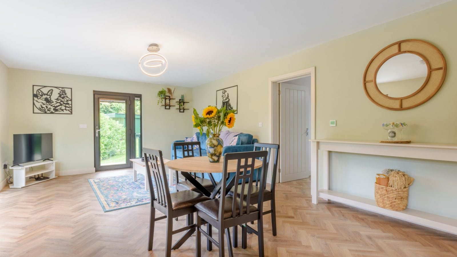 A living room with a round table, sunflowers, and a blue sofa at the Rowley Meadow Secret Waterside Lodges.