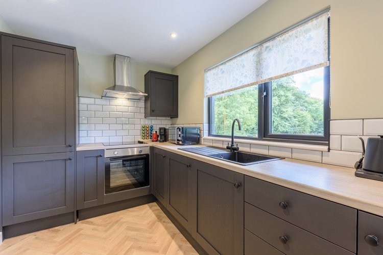 Modern kitchen with dark cabinets, stainless steel appliances, and a wood countertop. A large window offers a picturesque view of Rowley Meadow, seamlessly blending nature's beauty with contemporary design.