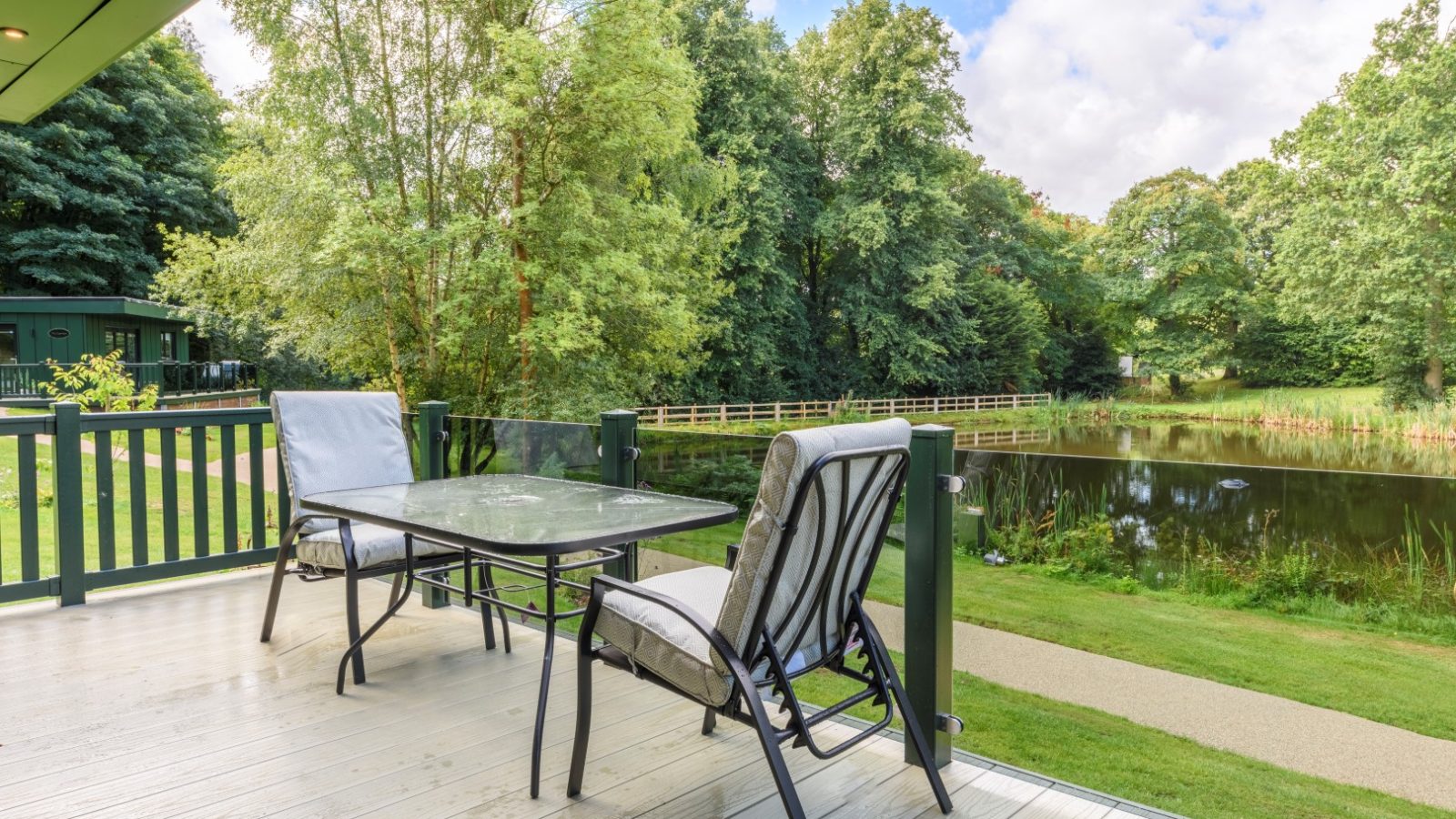 Outdoor patio at Rowley Meadow features a glass table, two cushioned chairs, and overlooks the secret Waterside Lodges pond.