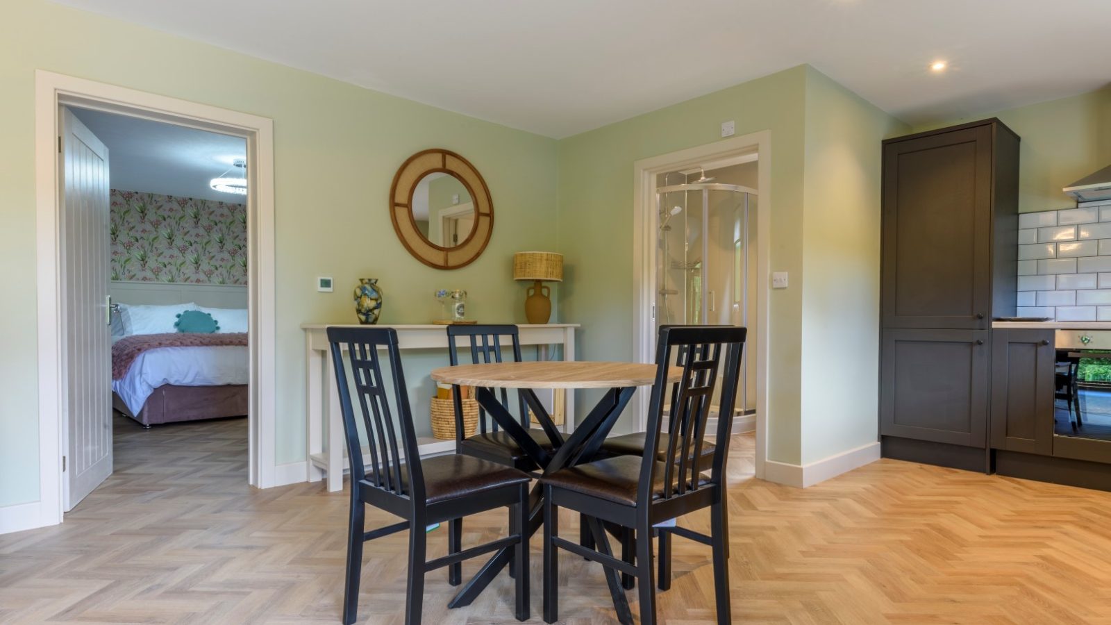 Dining area with a round table and four chairs, near the Secret Waterside Lodges and a bedroom with a pink floral bedspread.