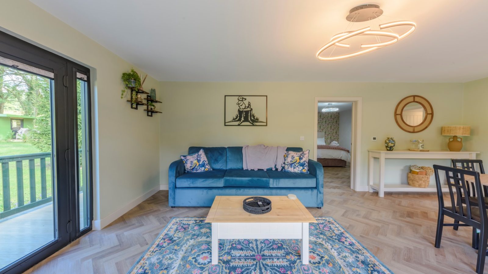 A living room with a blue sofa, patterned rug, and glass doors leading to the serene Rowley Meadow view.