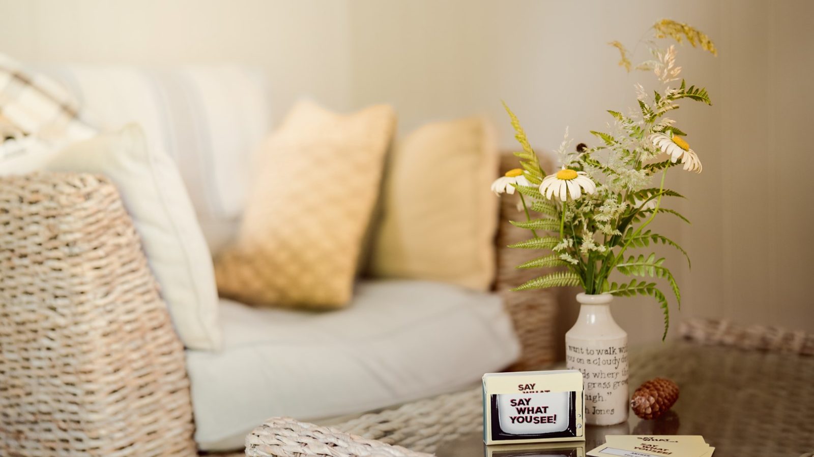 A cozy living room with wicker furniture, a vase of flowers, and a small sign reading 