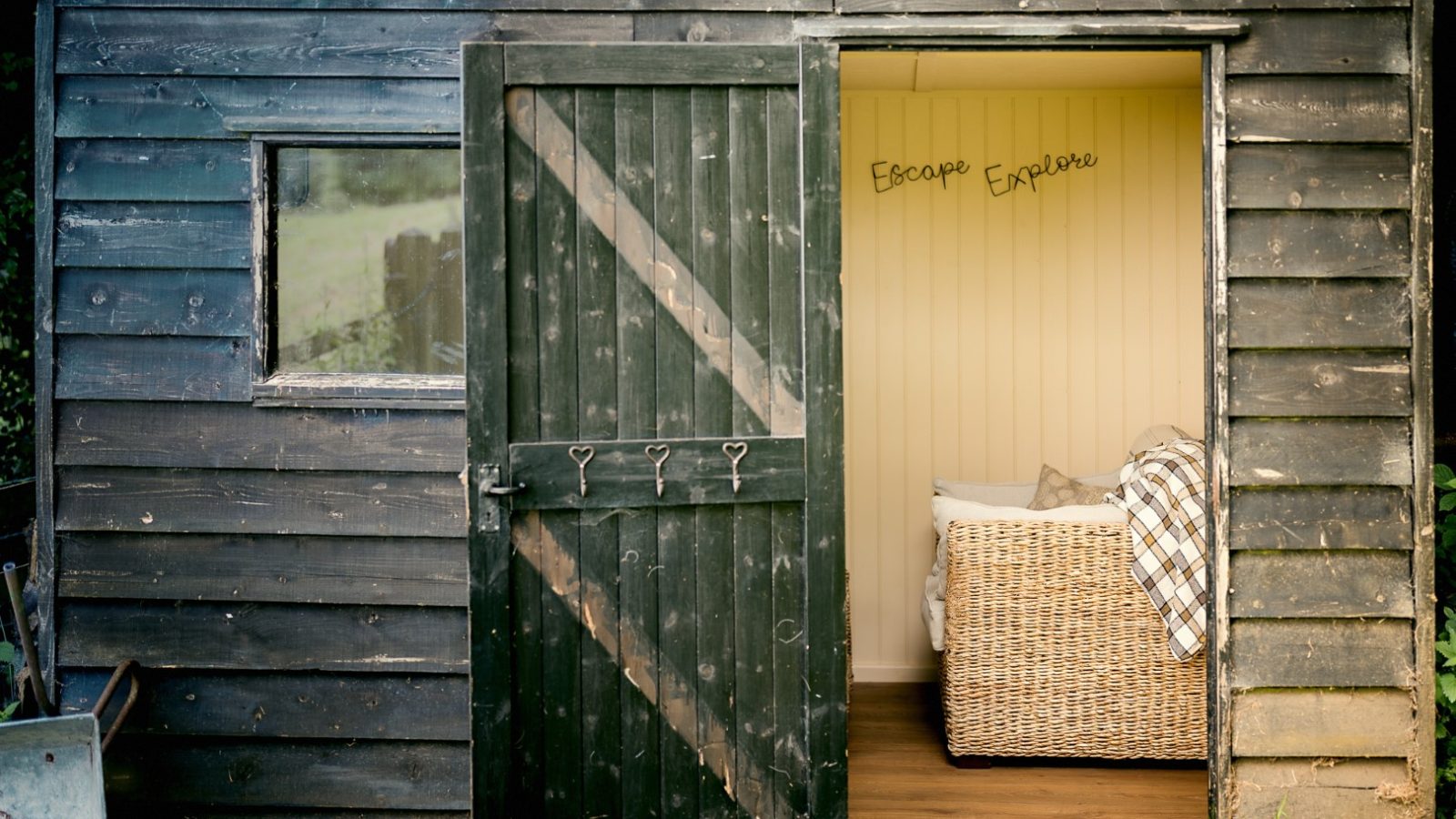 A wooden shed with an open door reveals a wicker chair and blanket inside. The wall has 