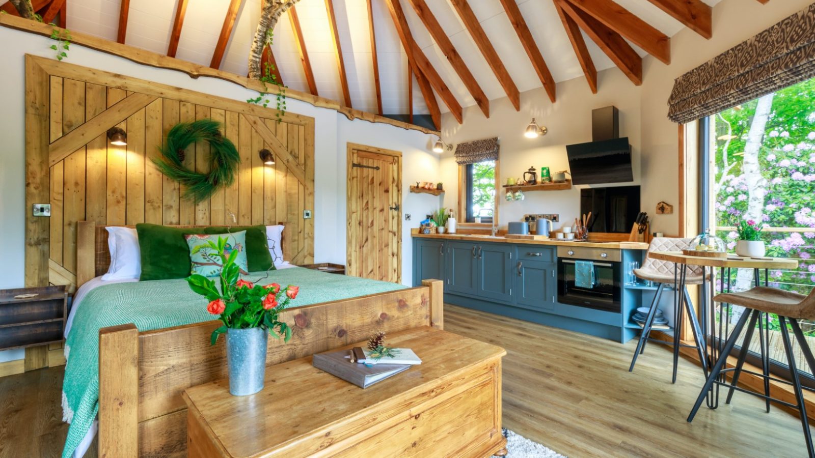 Treetop Hideaway: Cozy cabin interior with wooden bed, kitchenette, and rustic decor. Natural light pours through large windows.