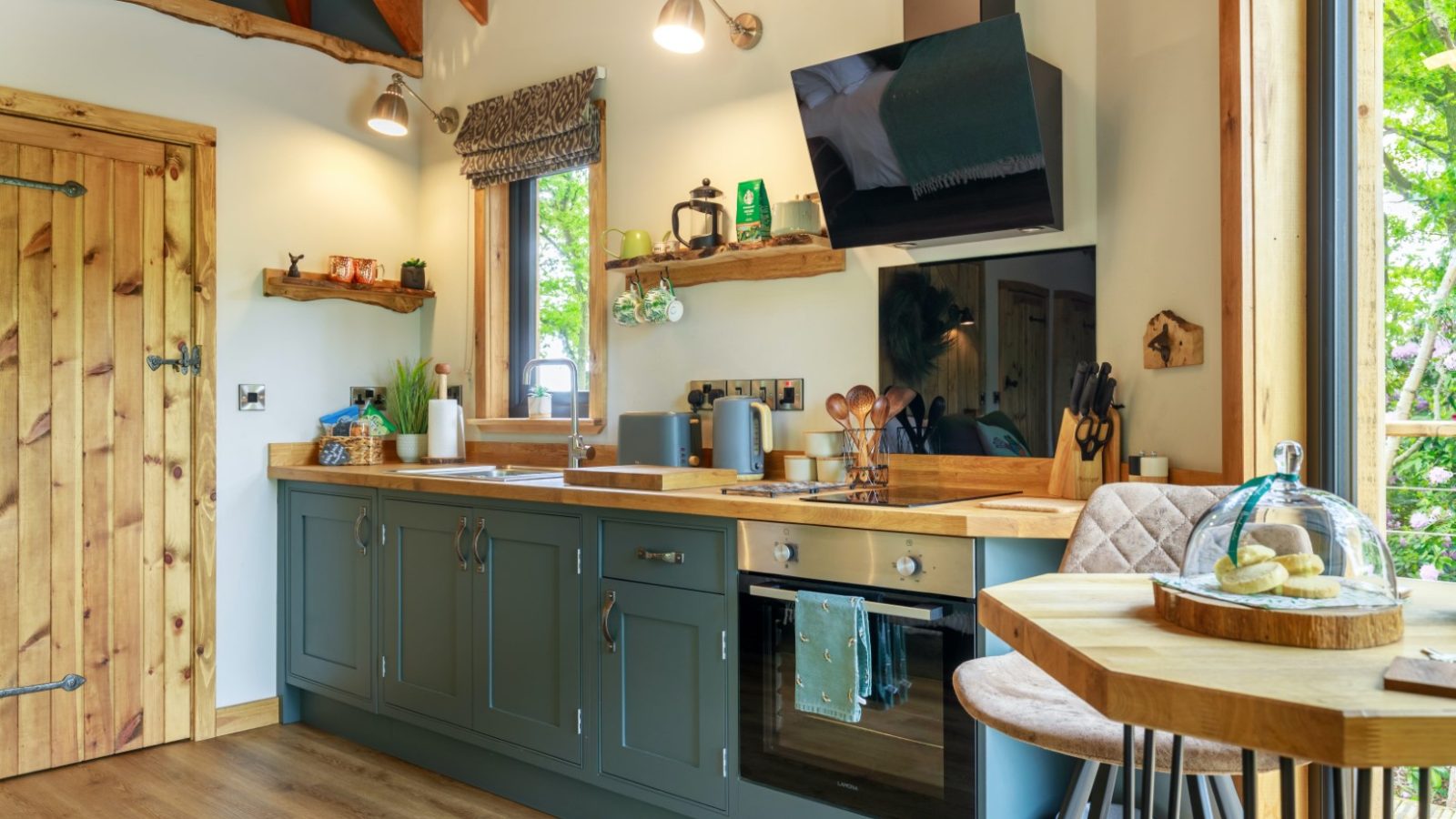 Cozy kitchen with green cabinets, wooden countertops, and modern appliances in a Treetop Hideaway featuring a small dining set.