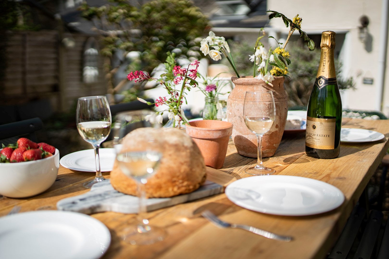 Outdoor table setting for a February Half Term Break with wine glasses, bread, strawberries, and champagne. Floral centerpiece included.