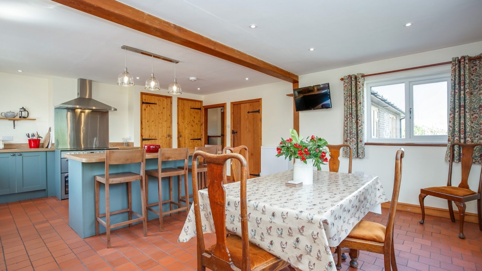 Brook Cottage boasts a spacious kitchen with a wooden dining table, central island, stove, light blue cabinets, and floral curtains.