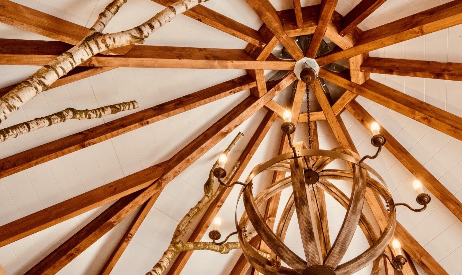 Treetop Hideaway: A wooden ceiling with exposed beams and branches, highlighting a spherical chandelier with lit bulbs.