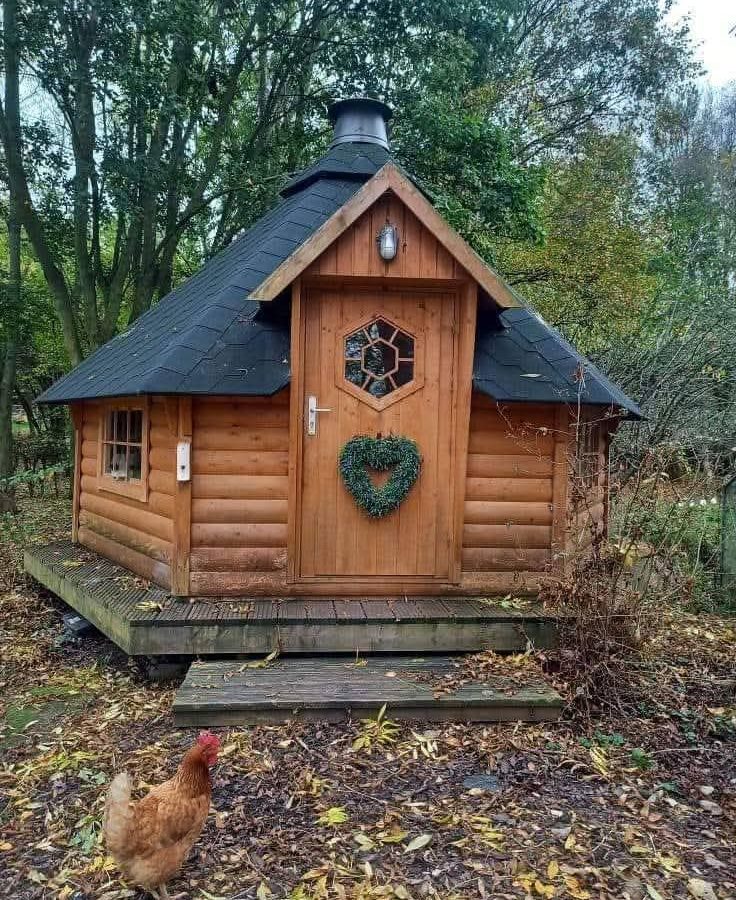 Hawthorn hideaway: A wooden cabin with a hexagonal window and heart-shaped wreath, a chicken stands guarding the entrance.