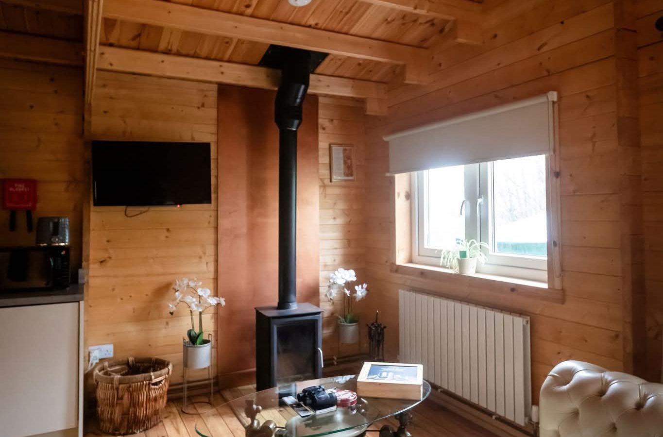 Cozy wooden cabin interior at Hawthorn Hideaway with a sofa, wood stove, wall-mounted TV, and decor-laden coffee table.