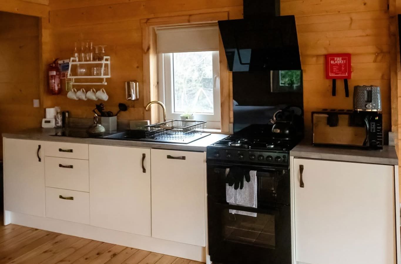 Hawthorn Hideaway: A wooden kitchen interior with a black stove, white cabinets, and polished wood floors.