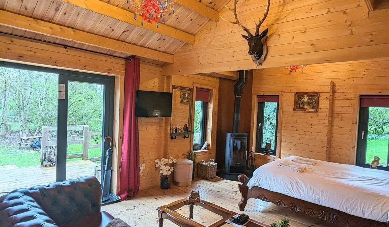 Hawthorn Hideaway's cozy cabin boasts a bed, sofa, antler decor, chandelier, and large windows overlooking lush greenery.