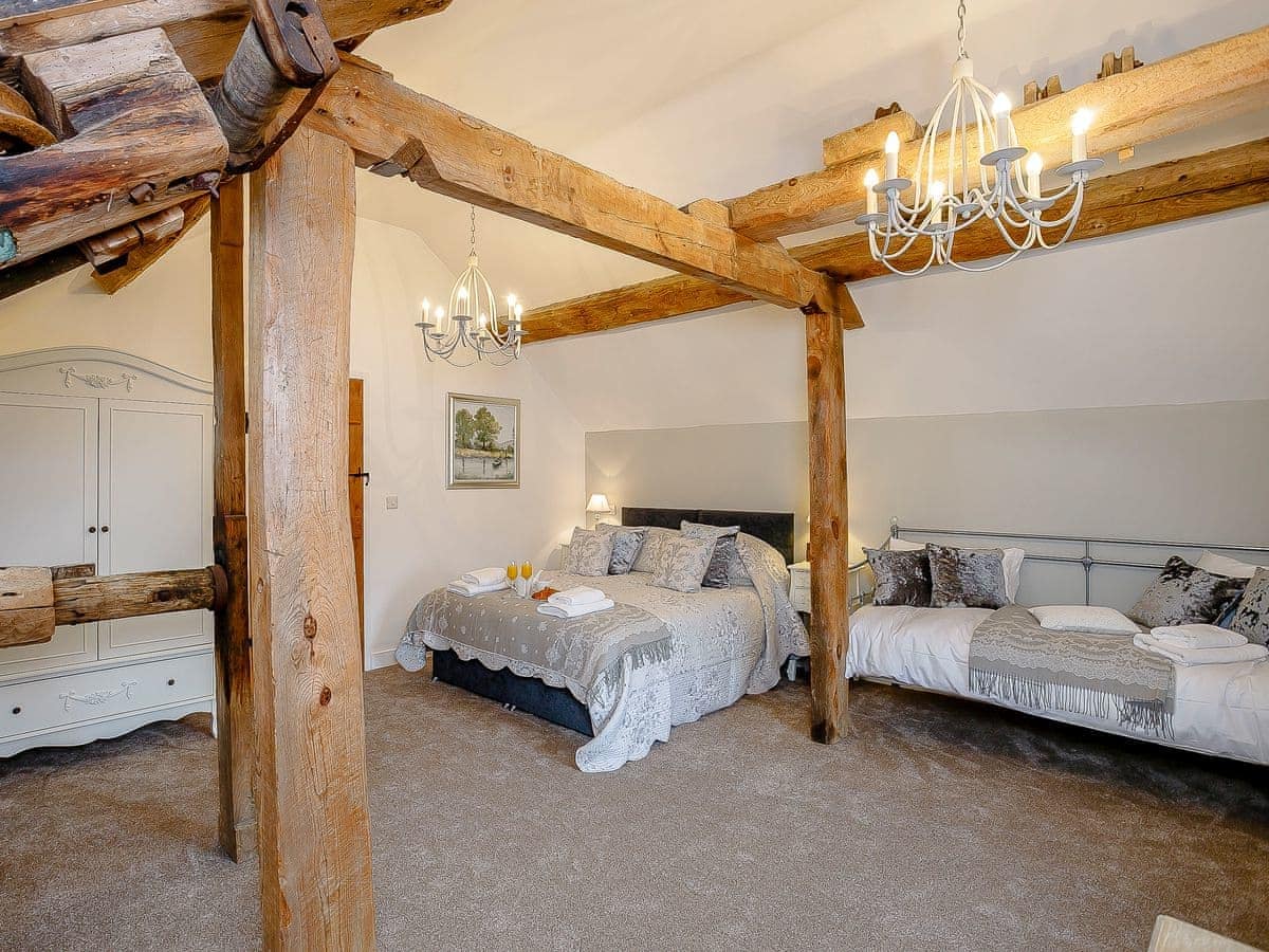 Rustic bedroom with exposed beams, two beds, a chandelier, wardrobe, and a decorative painting of The Water Mill.