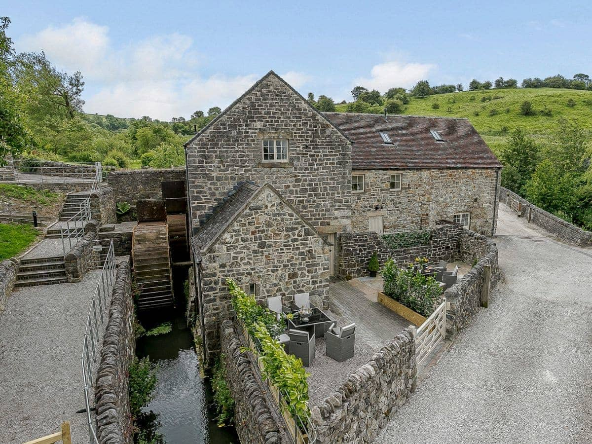 The Water Mill, an old stone building with two levels and a waterwheel, sits amid lush countryside and courtyard seating.