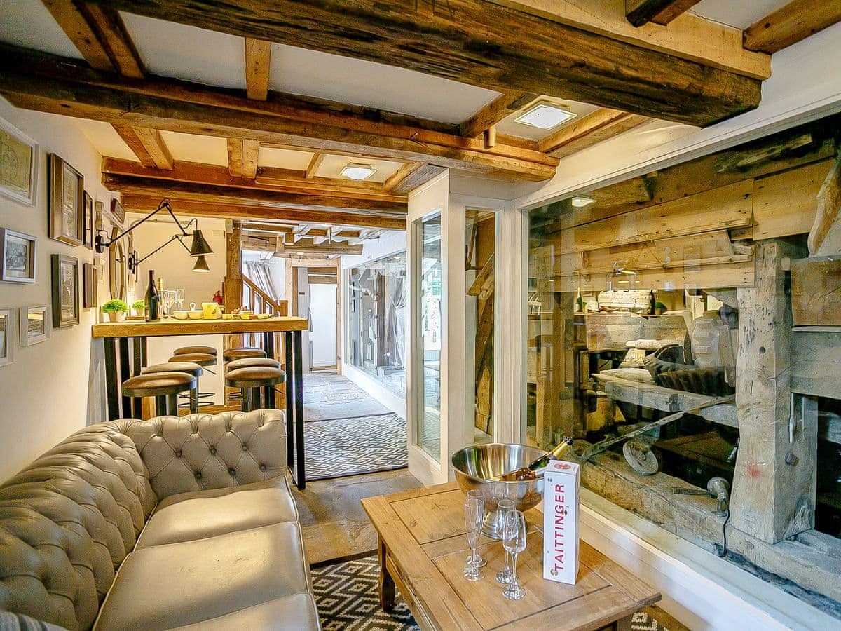 Cozy living room with wooden beams, a sofa, wall art, and bar table overlooking The Water Mill through a large window.