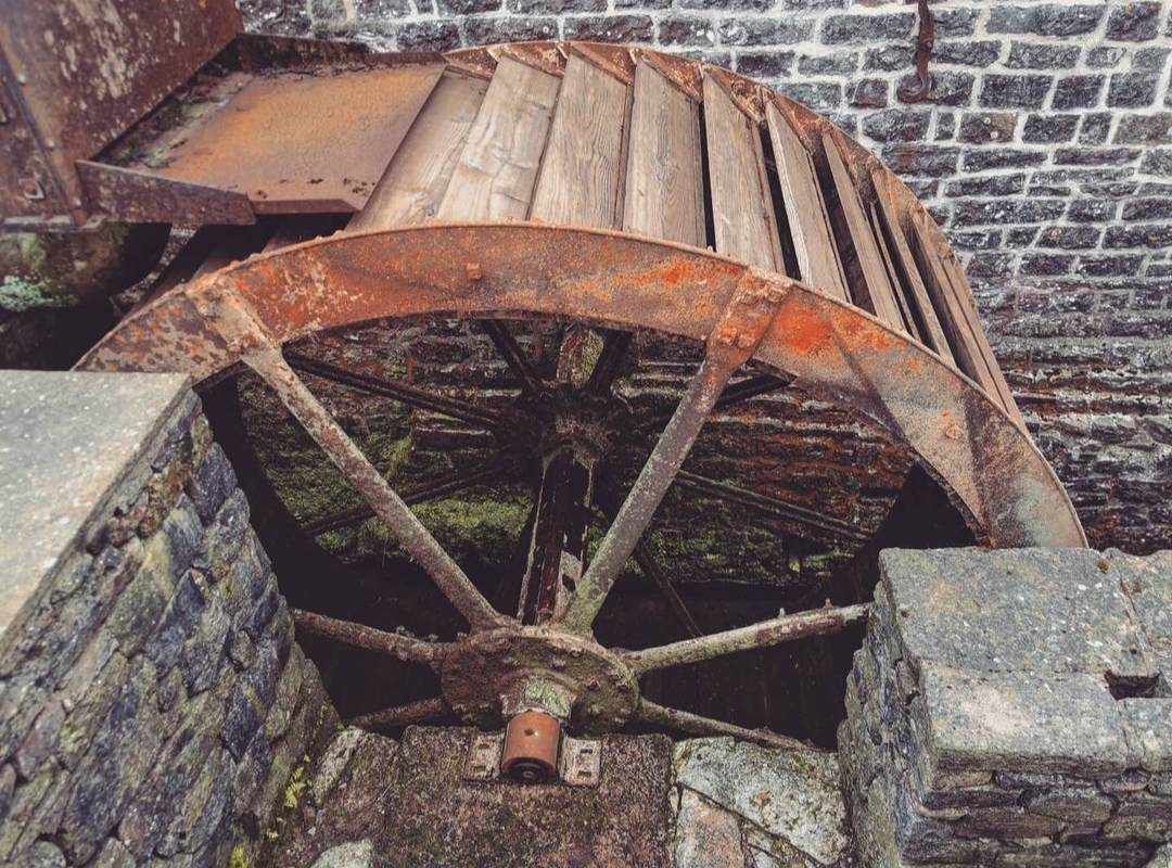 The Water Mill's rusty wheel clings to a stone building, embraced by old brick and moss-covered stones.