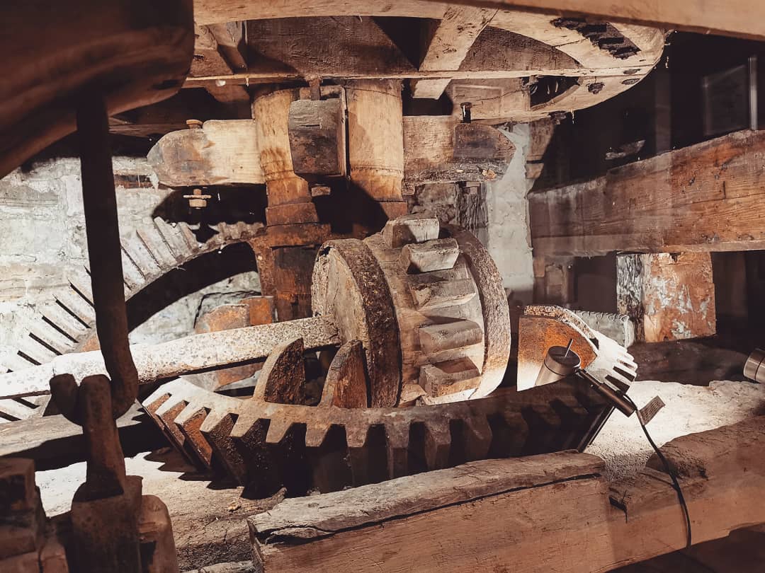 Close-up of large interlocking wooden gears and axles inside The Water Mill, showing mechanical components and texture.