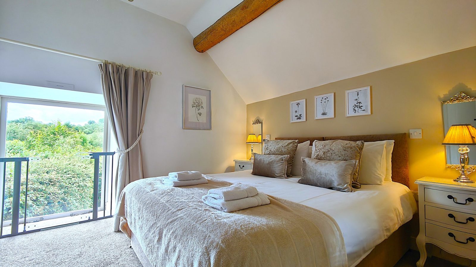 A cozy bedroom with a large bed, lamps, and a view of The Water Mill, framed by three decorative pictures.