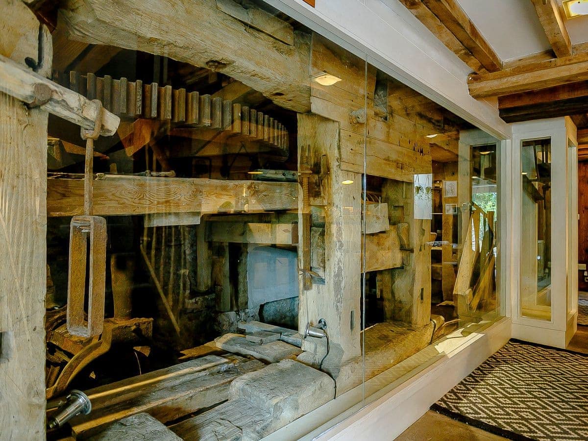 Antique wooden machinery in glass within The Water Mill, featuring gears, large beams, and a patterned floor.