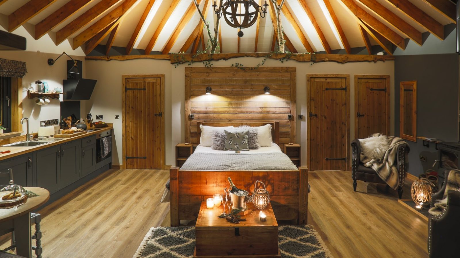 Cosy Treetop Hideaway with vaulted wood ceiling, bed, rustic decor, and lantern-lit kitchen area.