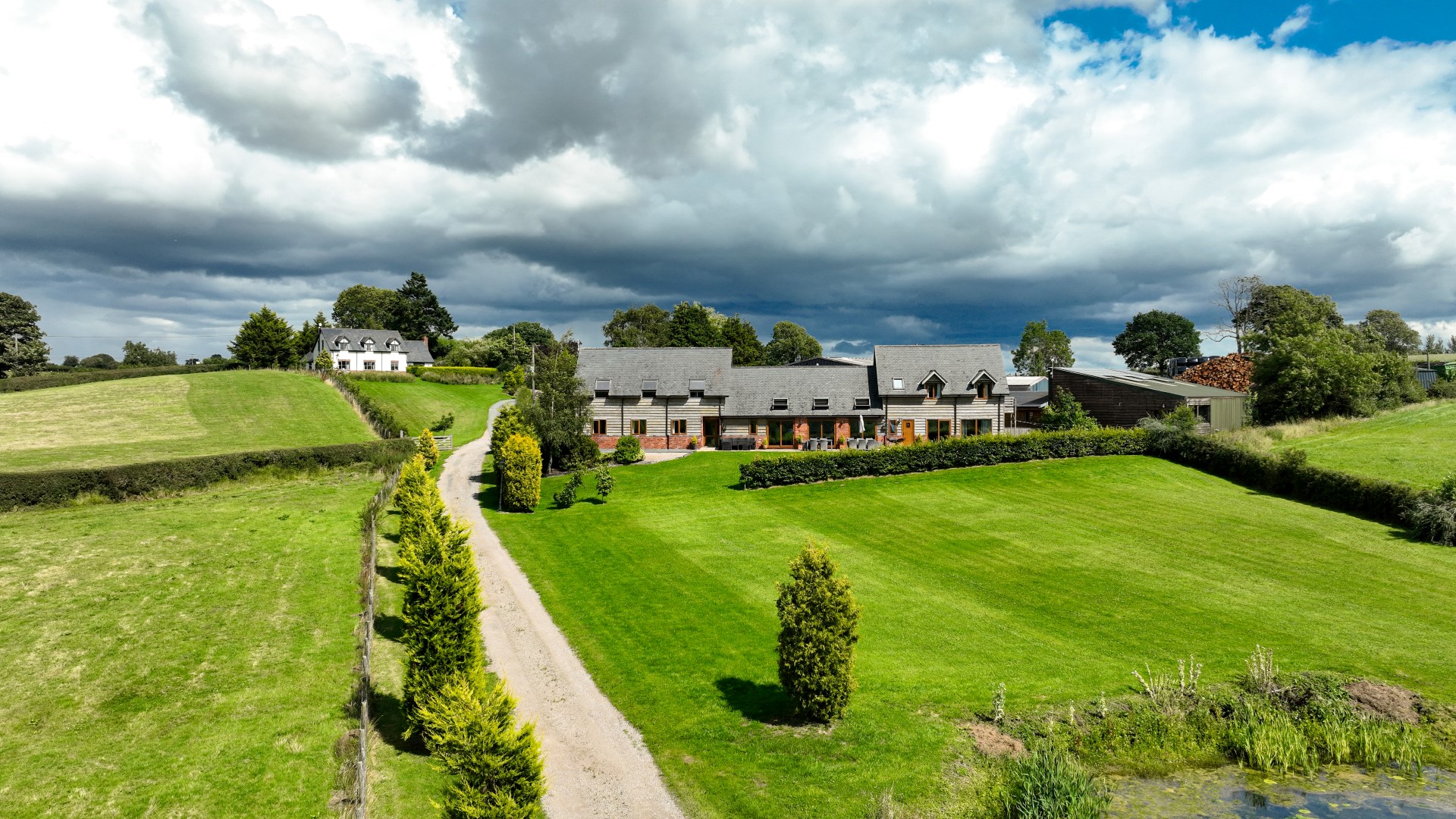 Aerial view of a country house, ideal for February half-term breaks, with a gray roof, landscaped lawn, trees, and gravel driveway.