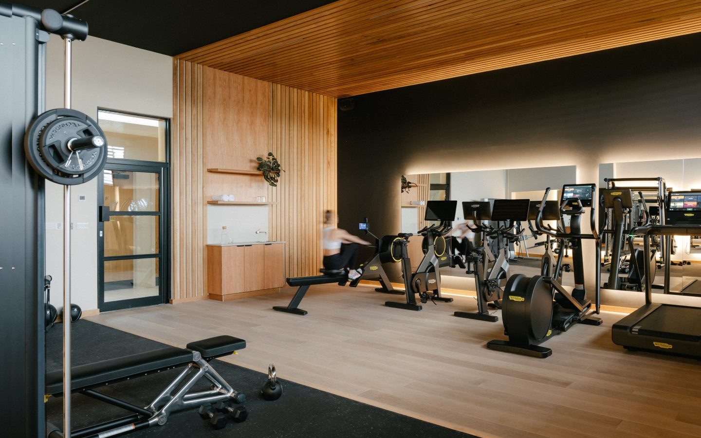 Modern Highcliffe gym interior with wooden ceiling, various exercise equipment including treadmills, rowing machines, and weights.