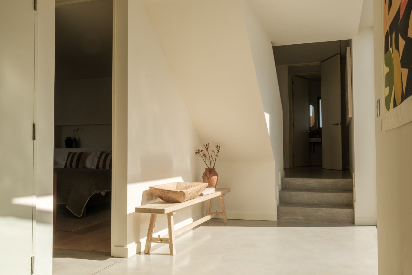 Minimalist Highcliffe interior with natural light, wooden bench, flowers in vase, and abstract art near an open doorway and steps.