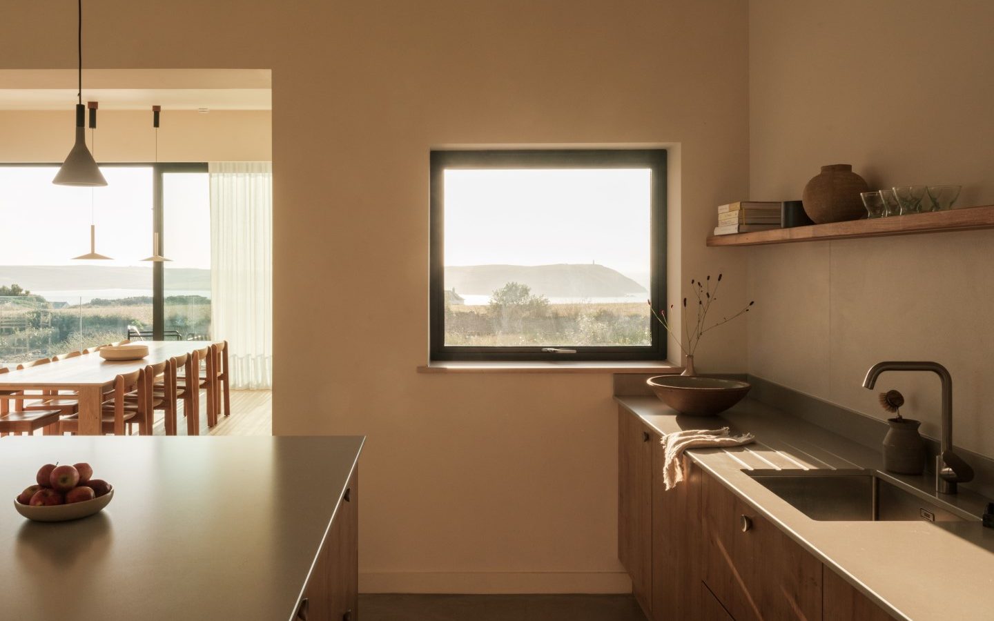 Minimalist Anterre kitchen with wooden cabinets, central island, and ocean view. Dining table visible in the next room.