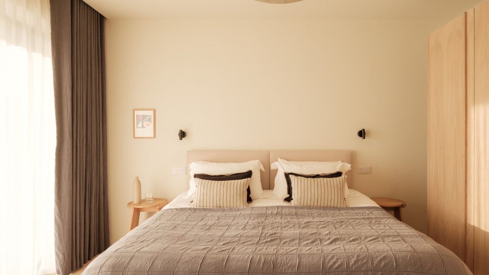 A minimalist bedroom in Highcliffe features a neatly made bed, two side tables, a pendant light, and soft natural lighting.