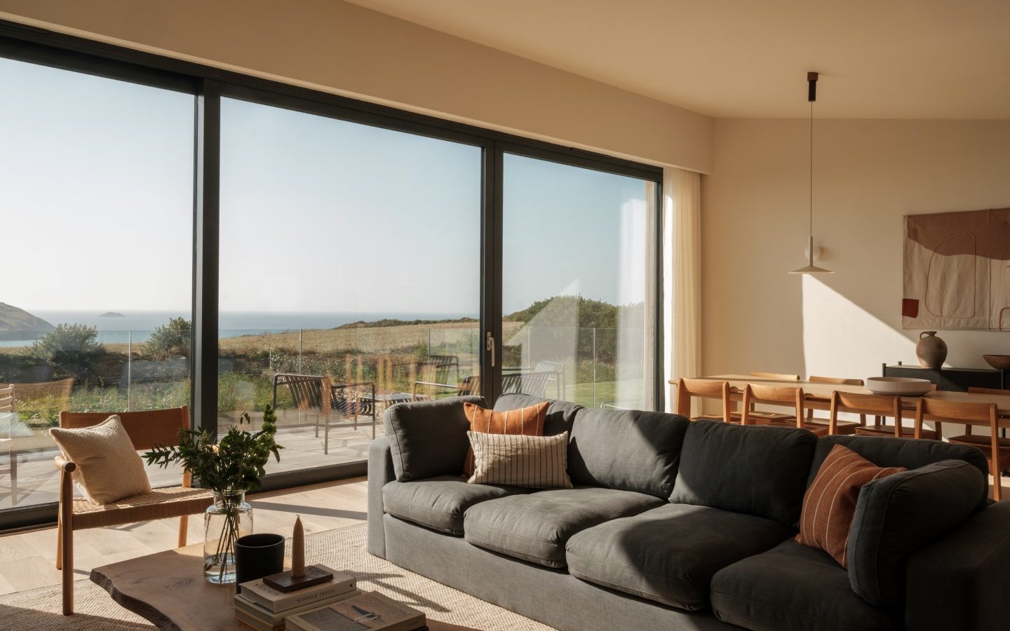 Modern living room with Anterre style, featuring large glass doors, green sofa, wooden table, and outdoor patio view.