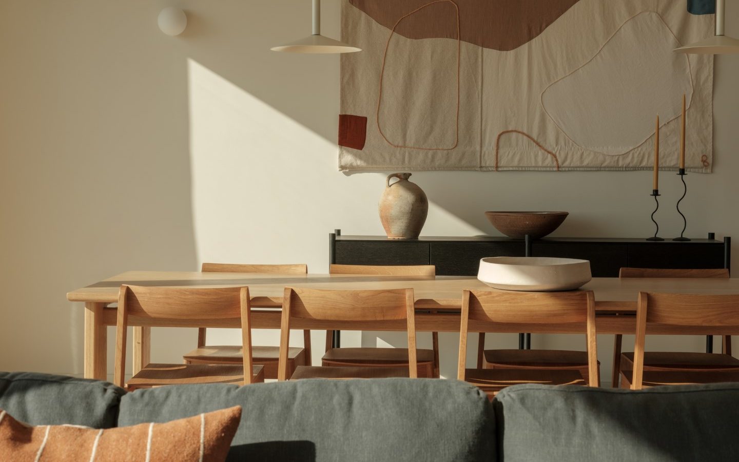 Minimalist dining area with a wooden table, Highcliffe chairs, abstract wall art. An Anterre vase sits on the sideboard.