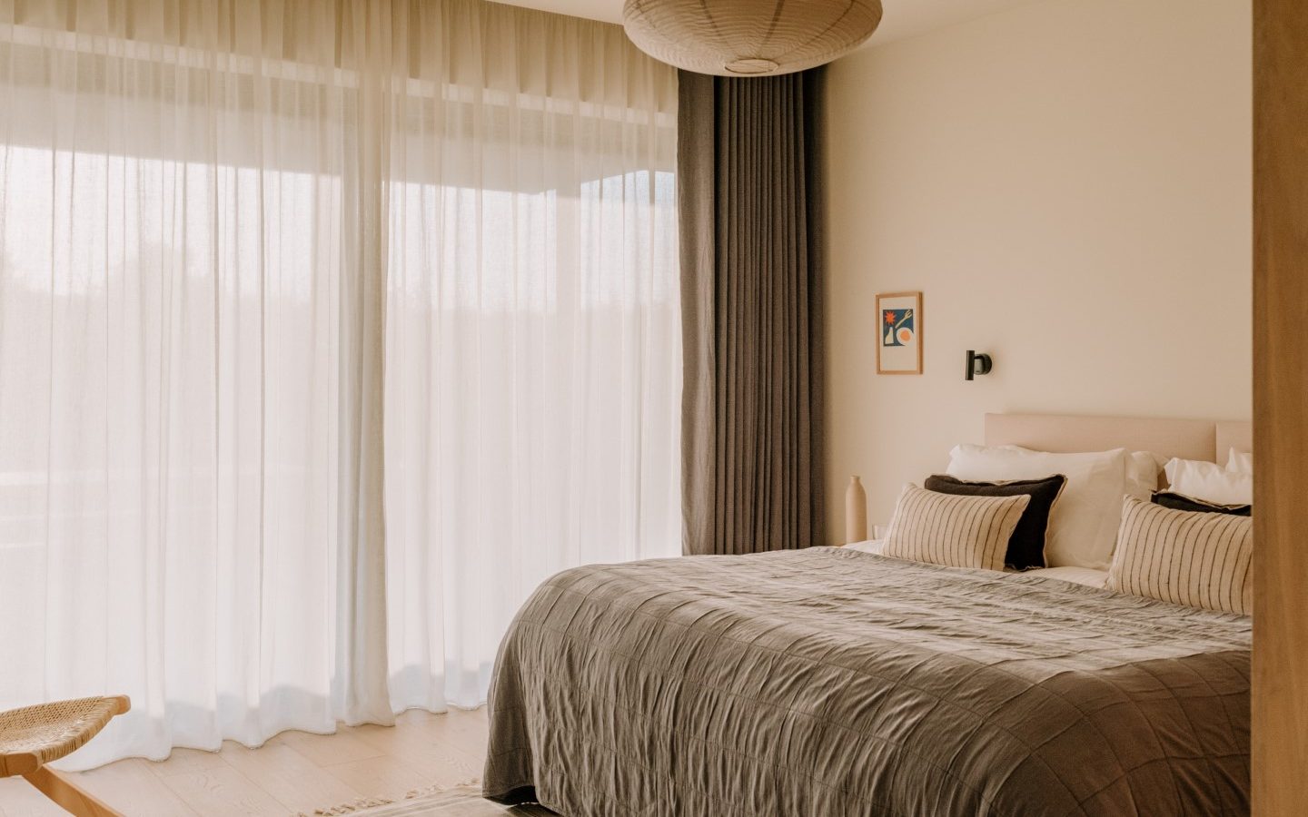 Minimalist Highcliffe bedroom with a large bed, neutral bedding, sheer curtains, a pendant light, and a small wall art piece.