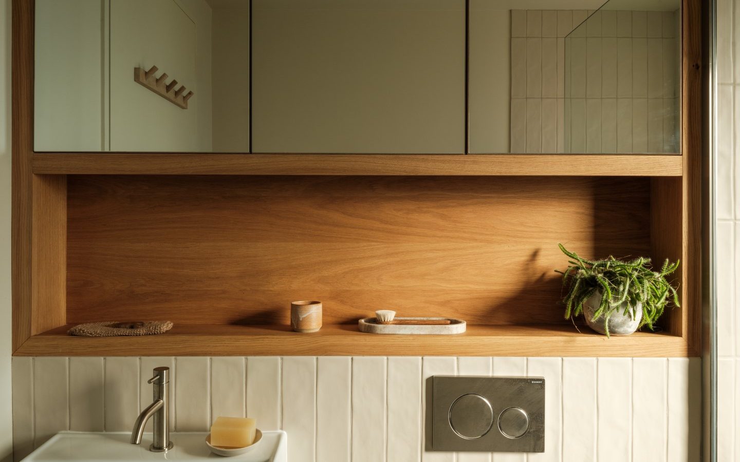 Minimalist bathroom with Anterre wooden shelf, mirror cabinet, sink, faucet, and plant. Tiled backsplash and soap dish visible.