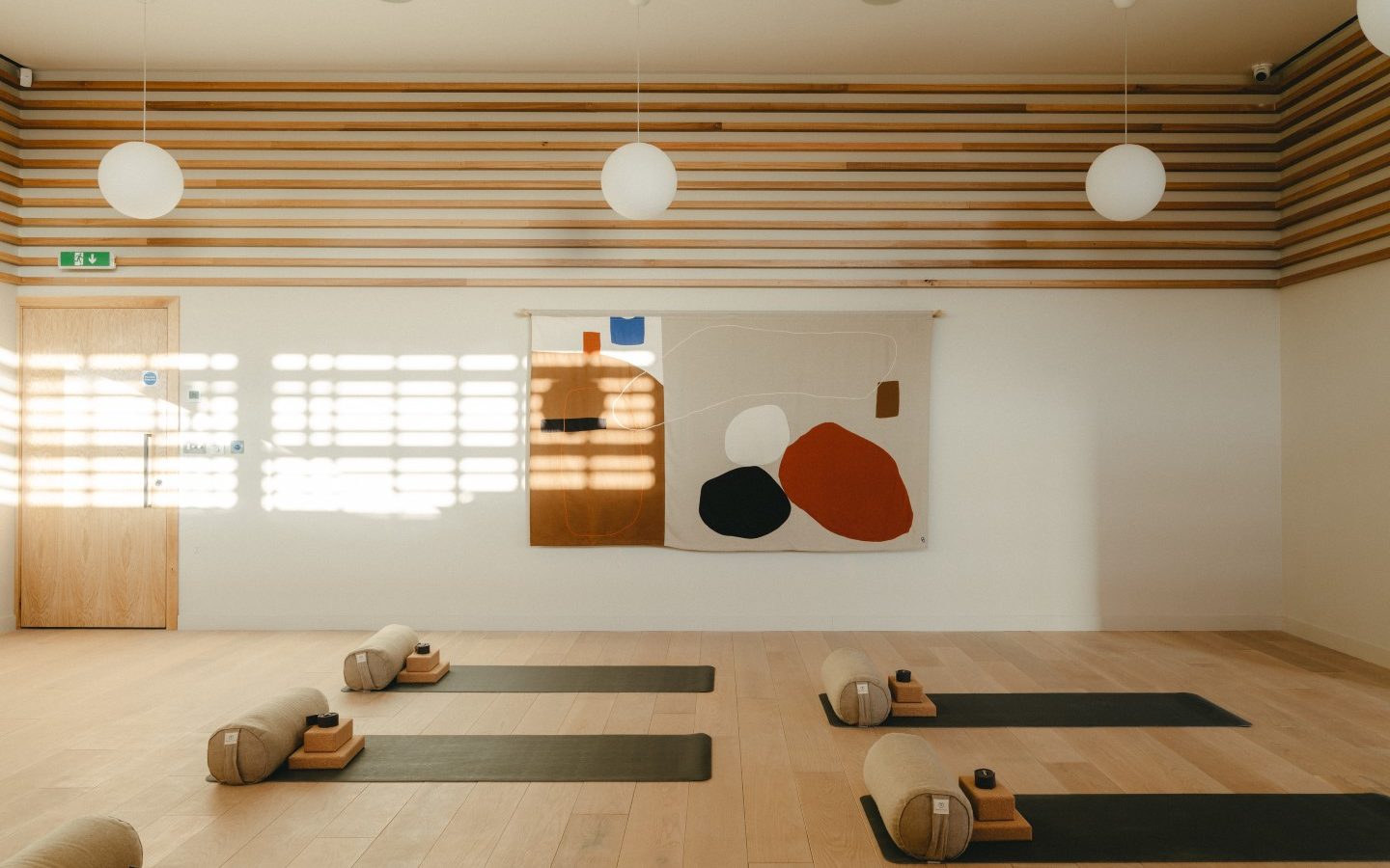 A sunlit yoga studio in Highcliffe with mats, bolsters, and blocks aligned on the floor. Art and round ceiling lights create ambiance.