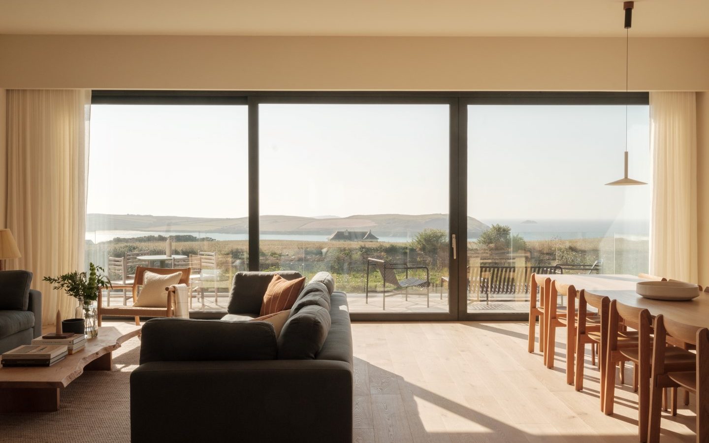 Bright living room with a sofa, dining table, and large glass doors opening to a patio. Overlooks Anterre's sea and hills beyond.