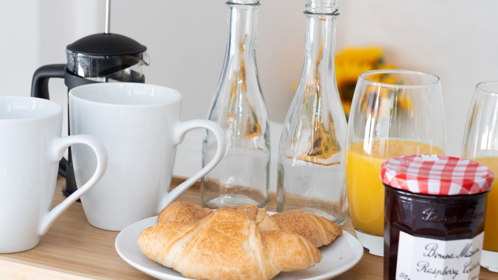 Breakfast setting in Abersoch with croissants on a plate, two glasses of orange juice, a French press, and two mugs.