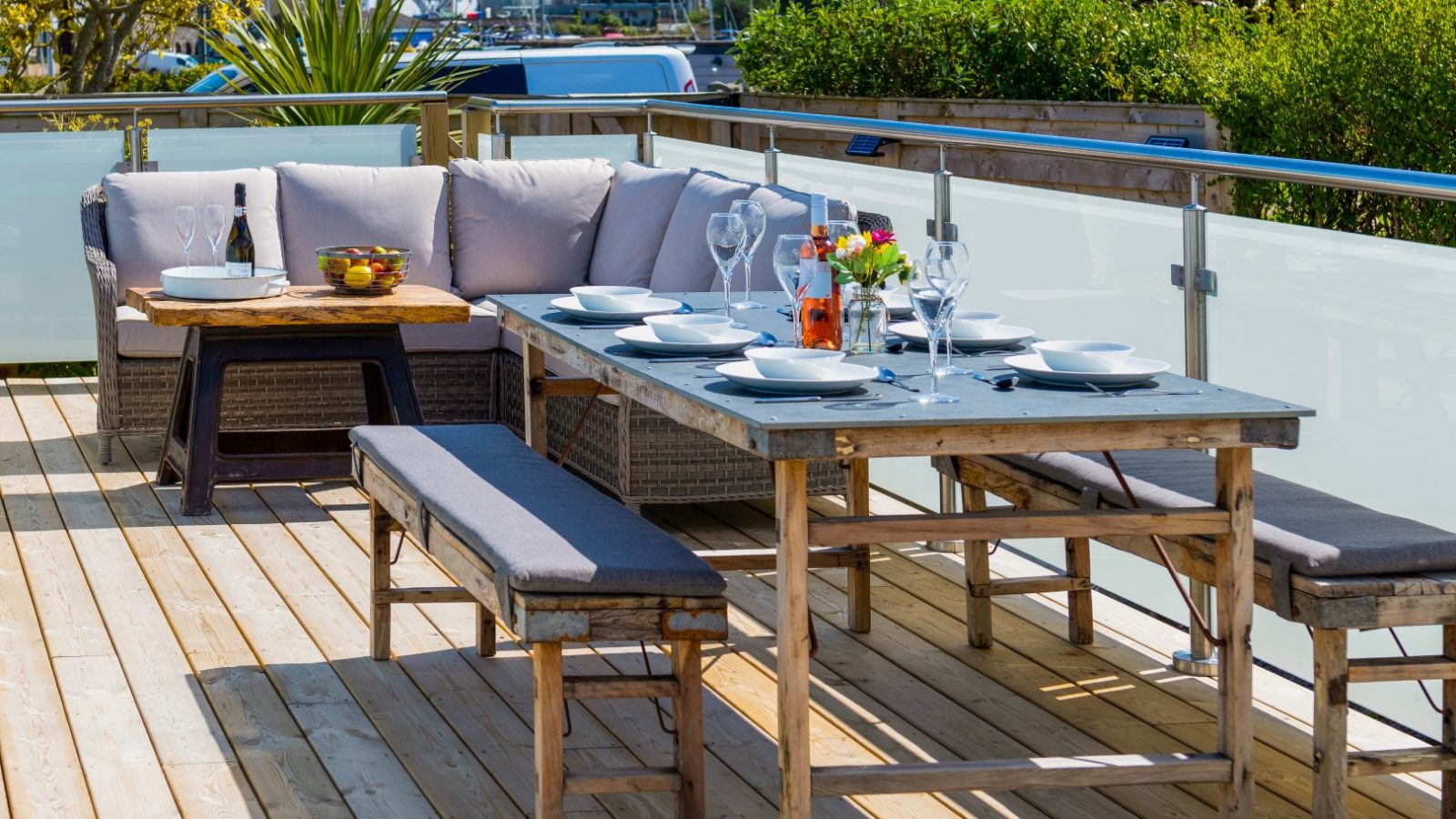 Arfor outdoor dining setup with a wooden table, benches, and a sofa on a deck near Abersoch. Set with plates, glasses, and flowers.