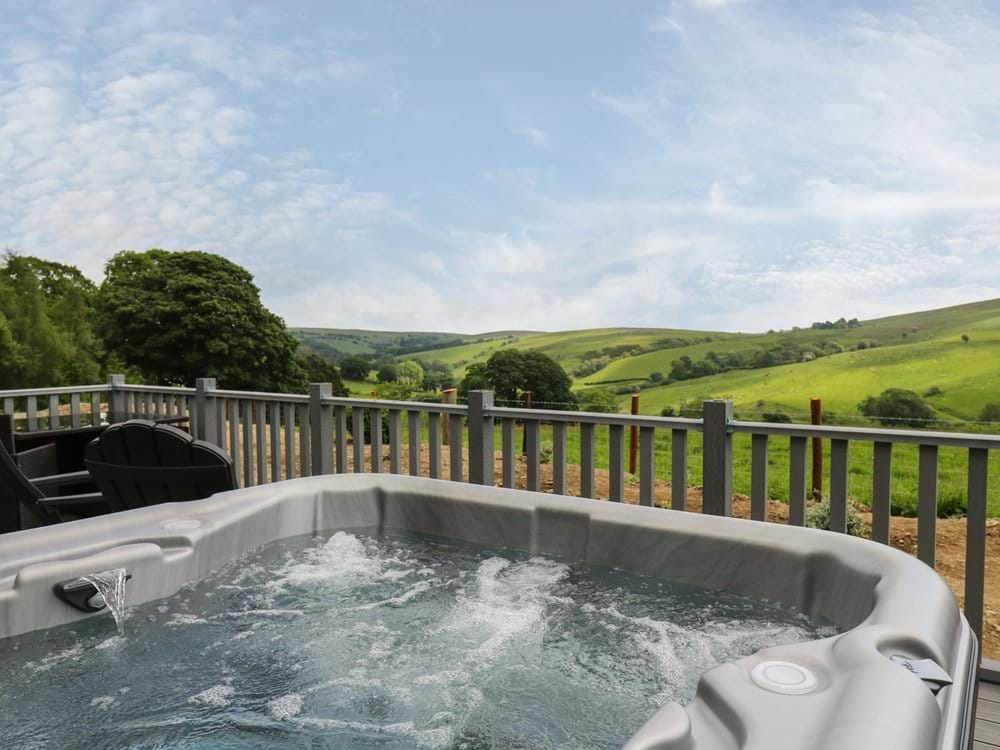 Hot tub with bubbling water on a deck, perfect for digital detox stays, overlooking scenic green hills and trees under a blue sky.