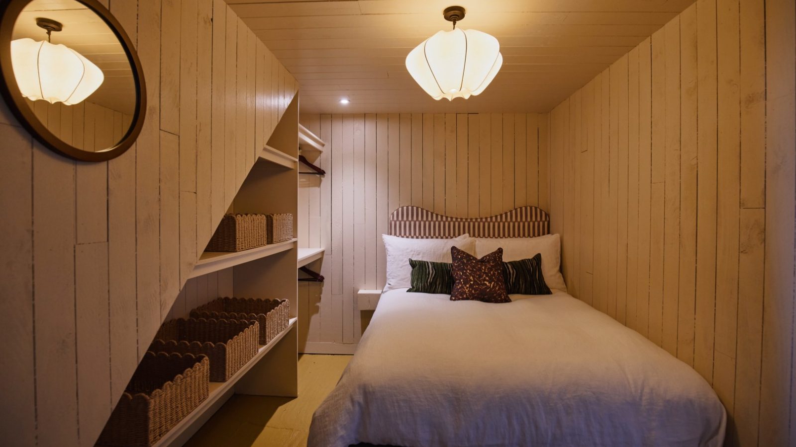 Cozy Bonington Farm bedroom with a double bed, decorative pillows, a round mirror, and open shelving with wicker baskets.