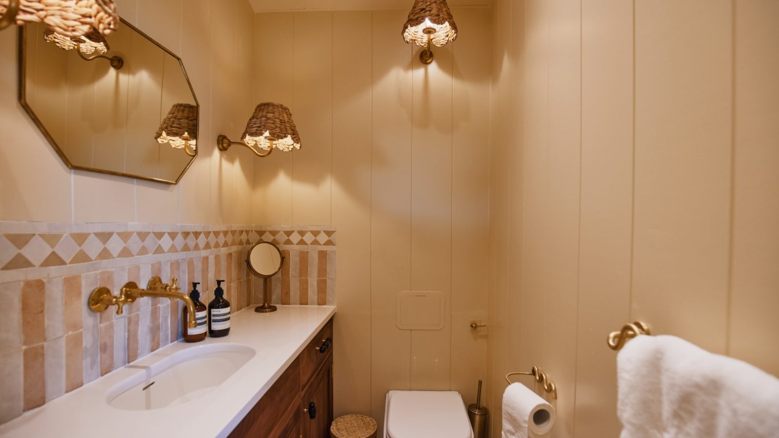 Cozy Bonington Farm bathroom with a sink, mirror, and toilet. Warm lighting and a brown-cream color scheme enhance charm.